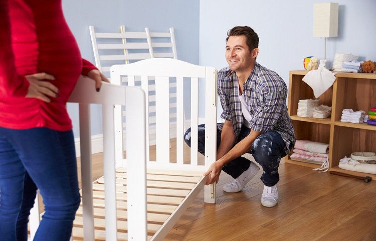 Couple With Pregnant Wife Assembling Cot In Nursery